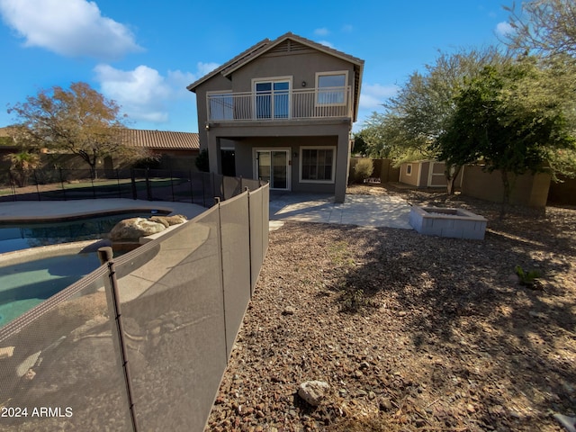 back of house with a patio area, a balcony, a fenced in pool, and a storage shed