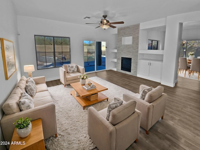 living room featuring hardwood / wood-style flooring, ceiling fan, and a stone fireplace