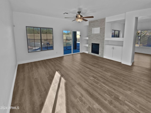 unfurnished living room featuring ceiling fan, a stone fireplace, dark wood-type flooring, and built in shelves