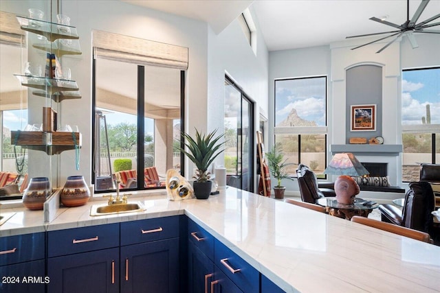 interior space featuring ceiling fan, blue cabinets, sink, a fireplace, and light stone countertops