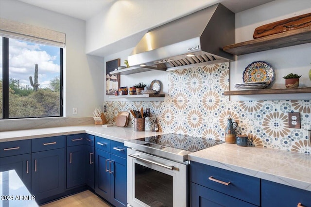 kitchen featuring decorative backsplash, wall chimney exhaust hood, stainless steel range with electric cooktop, and blue cabinetry