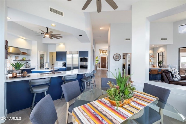 dining space with light hardwood / wood-style flooring, a towering ceiling, ceiling fan, and sink