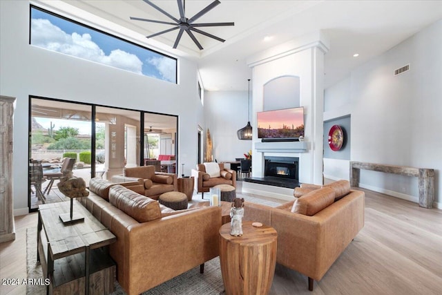 living room featuring ceiling fan, light wood-type flooring, and a towering ceiling