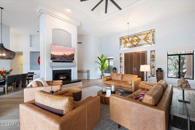 living room with light hardwood / wood-style flooring, a towering ceiling, and ceiling fan with notable chandelier