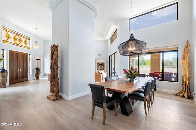 dining space featuring light hardwood / wood-style flooring, a towering ceiling, and a notable chandelier