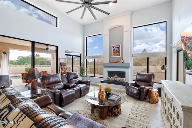 living room featuring light wood-type flooring, a high ceiling, a large fireplace, and ceiling fan