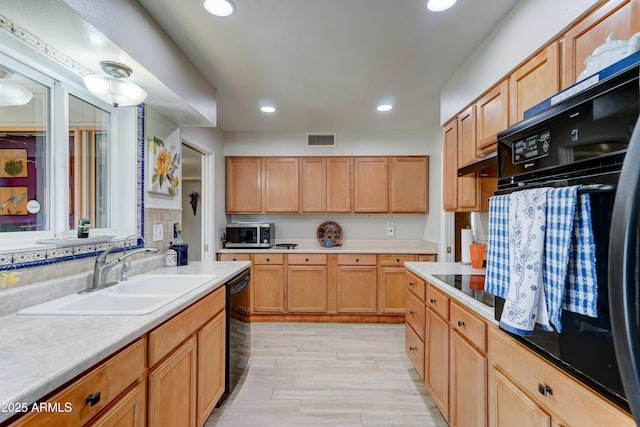 kitchen featuring light countertops, visible vents, light wood-style flooring, a sink, and black appliances