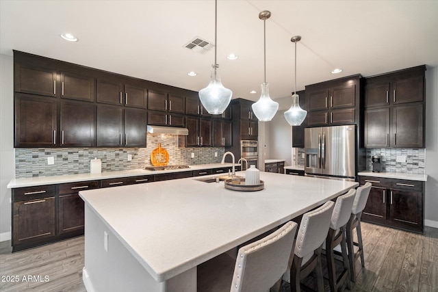 10702 E Sheffield Dr, Mesa, AZ 85212 - kitchen featuring appliances with stainless steel finishes, sink, hanging light fixtures, dark brown cabinets, and a center island with sink