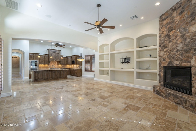 living area featuring built in features, a fireplace, arched walkways, and a ceiling fan