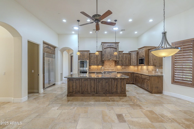 kitchen with arched walkways, a kitchen island with sink, stainless steel appliances, a high ceiling, and tasteful backsplash