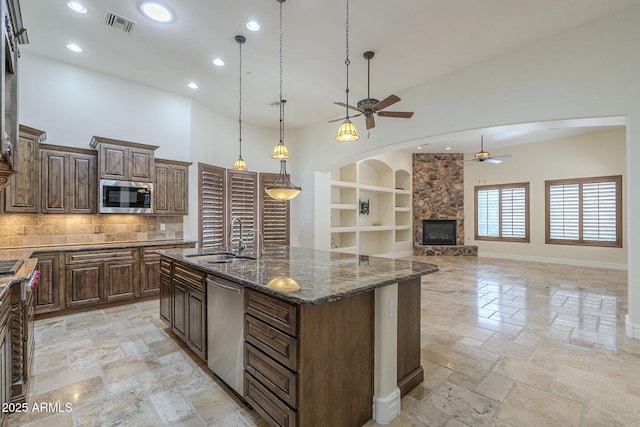 kitchen featuring arched walkways, stone tile flooring, appliances with stainless steel finishes, a sink, and a stone fireplace