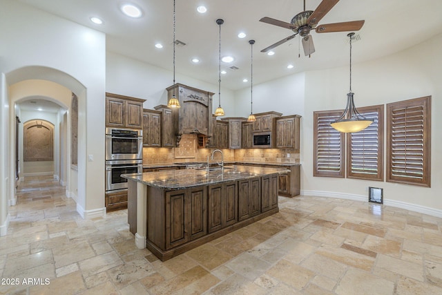 kitchen featuring arched walkways, stone tile floors, a high ceiling, appliances with stainless steel finishes, and decorative backsplash