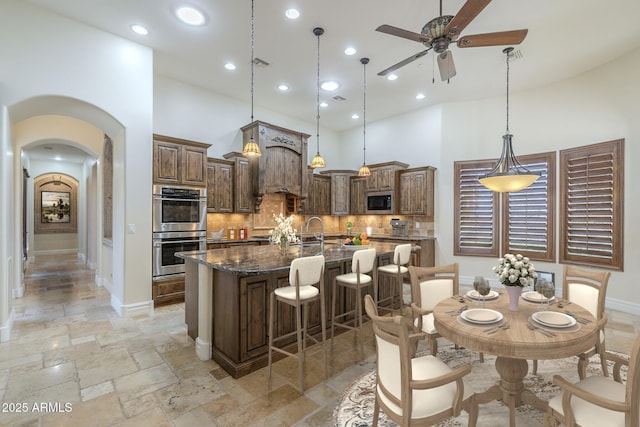 kitchen with arched walkways, stone tile flooring, decorative backsplash, a high ceiling, and appliances with stainless steel finishes