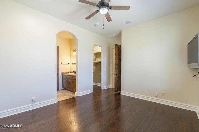 interior space with baseboards, arched walkways, a walk in closet, and wood finished floors