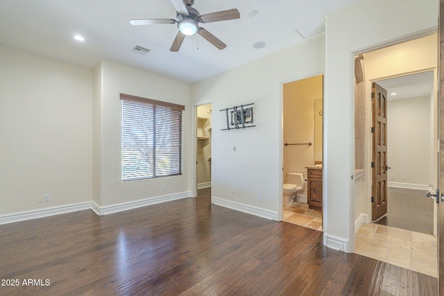 unfurnished bedroom with baseboards, visible vents, ensuite bath, wood finished floors, and a walk in closet