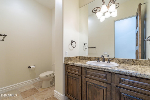 half bath with toilet, stone tile floors, baseboards, and vanity