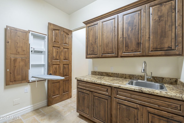 kitchen with dark brown cabinetry, a sink, baseboards, and light stone countertops