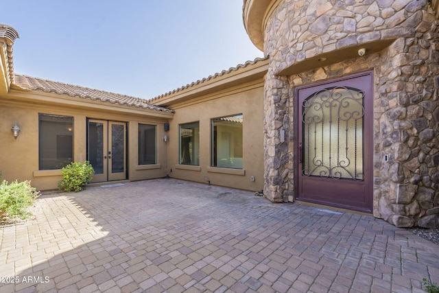 property entrance featuring stucco siding, stone siding, a patio, and french doors