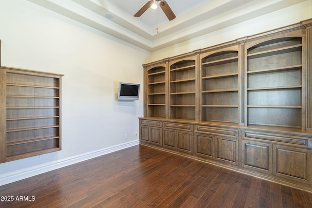 interior space with a tray ceiling, dark wood-style flooring, ceiling fan, and baseboards