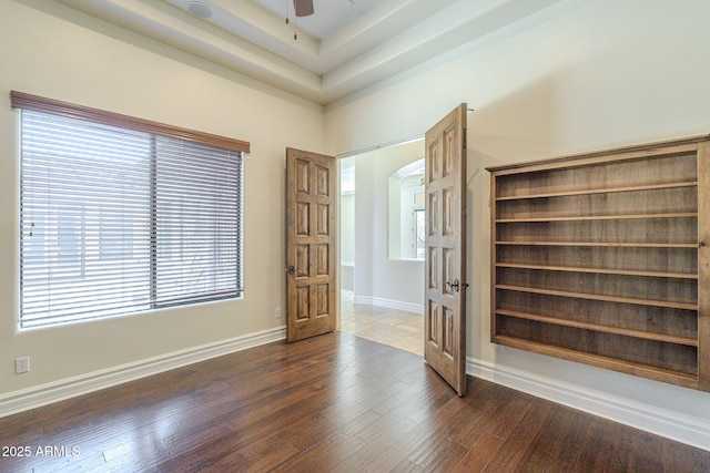 unfurnished room with baseboards, arched walkways, a ceiling fan, a raised ceiling, and dark wood-style floors