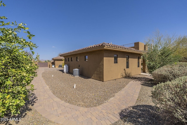 view of side of home featuring stucco siding, a tiled roof, and central air condition unit