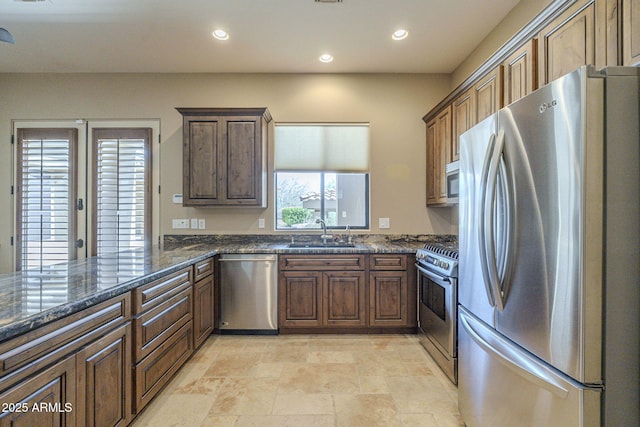 kitchen featuring recessed lighting, stainless steel appliances, a peninsula, a sink, and dark stone counters