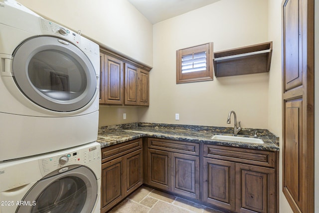 laundry area with stone finish floor, cabinet space, a sink, and stacked washer and clothes dryer