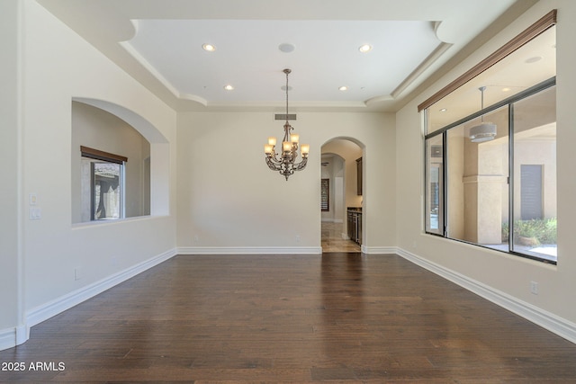 spare room with baseboards, a raised ceiling, dark wood finished floors, and a chandelier