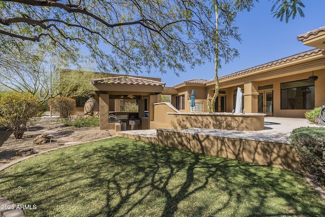 rear view of house with a lawn, area for grilling, a tiled roof, a patio area, and stucco siding