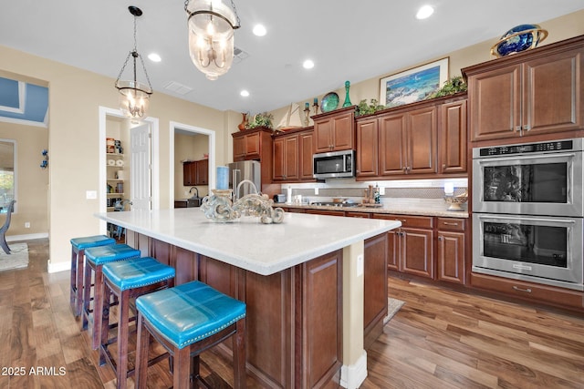 kitchen featuring a kitchen bar, an island with sink, appliances with stainless steel finishes, decorative light fixtures, and wood-type flooring