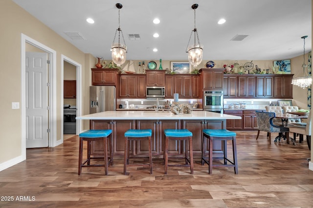 kitchen with pendant lighting, wood-type flooring, appliances with stainless steel finishes, a breakfast bar area, and a large island