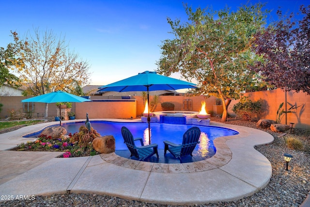 pool at dusk featuring a patio and an in ground hot tub