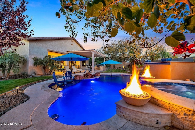 pool at dusk with an in ground hot tub and a patio