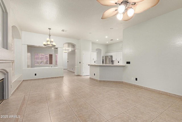 unfurnished living room with arched walkways, visible vents, light tile patterned flooring, baseboards, and ceiling fan with notable chandelier