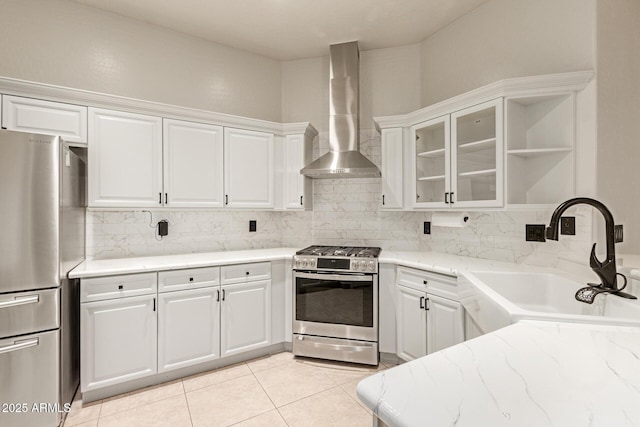 kitchen featuring stainless steel appliances, a sink, white cabinetry, wall chimney range hood, and backsplash