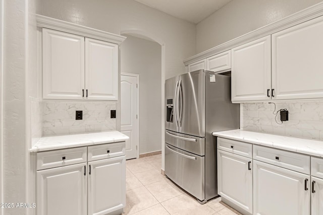 kitchen with arched walkways, white cabinetry, stainless steel refrigerator with ice dispenser, backsplash, and light tile patterned flooring