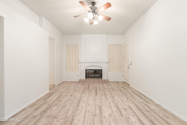 unfurnished living room featuring a ceiling fan, a glass covered fireplace, baseboards, and light wood finished floors