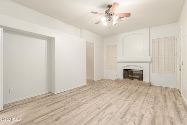 unfurnished living room featuring light wood finished floors, a glass covered fireplace, a ceiling fan, and baseboards