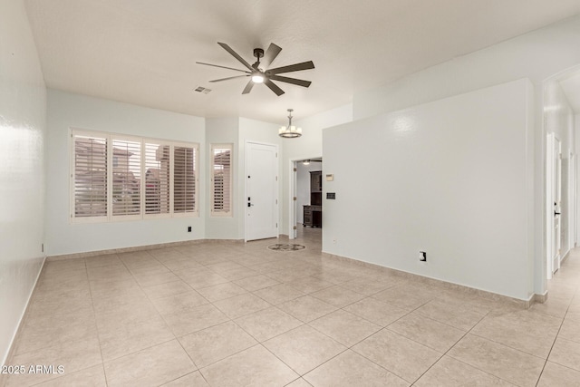 empty room featuring ceiling fan with notable chandelier, visible vents, baseboards, and light tile patterned flooring