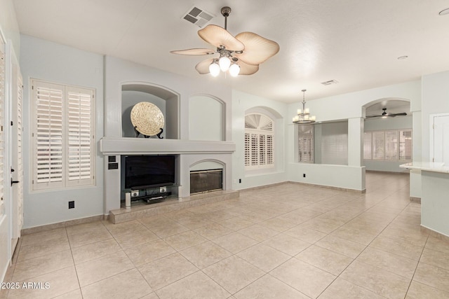 unfurnished living room with ceiling fan with notable chandelier, light tile patterned flooring, a tiled fireplace, and visible vents