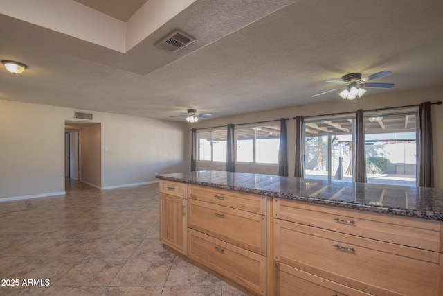 kitchen featuring a ceiling fan, dark stone countertops, visible vents, and baseboards