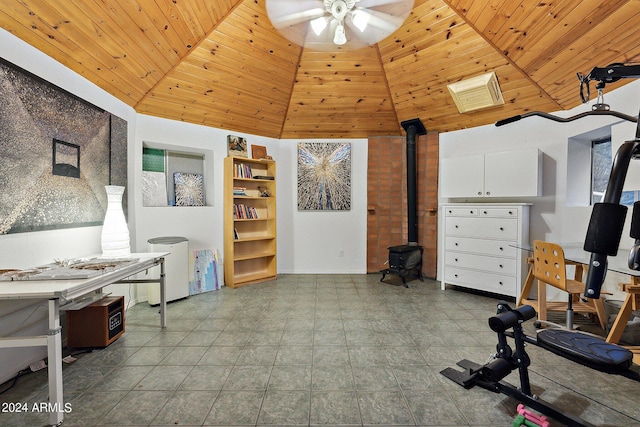 exercise area featuring ceiling fan, a towering ceiling, a wood stove, and wooden ceiling