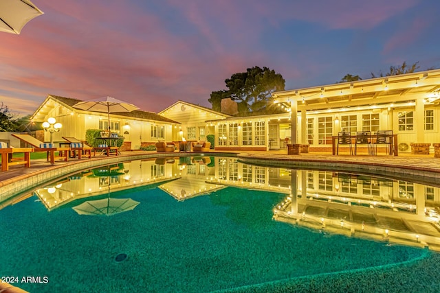 pool at dusk with a patio area and an outdoor pool