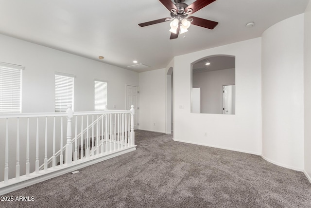 empty room featuring carpet, arched walkways, ceiling fan, a smoke detector, and baseboards