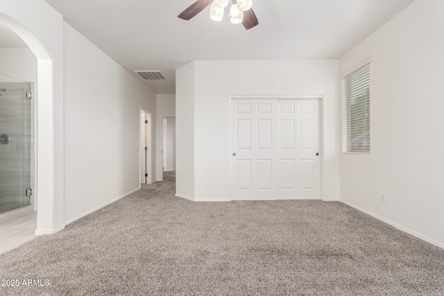 unfurnished bedroom featuring carpet, a closet, arched walkways, ensuite bath, and baseboards