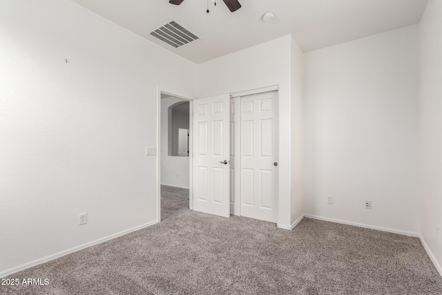 unfurnished bedroom featuring carpet, baseboards, a closet, ceiling fan, and arched walkways