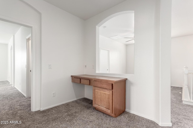 corridor with light carpet, a desk, arched walkways, and baseboards