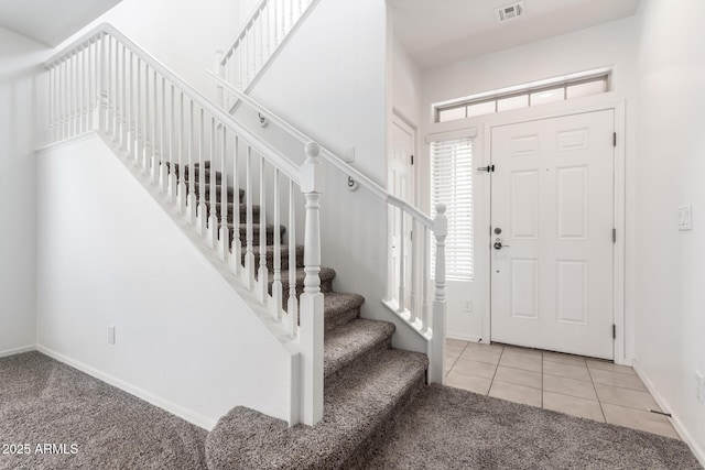 carpeted entrance foyer featuring stairs, baseboards, and tile patterned flooring