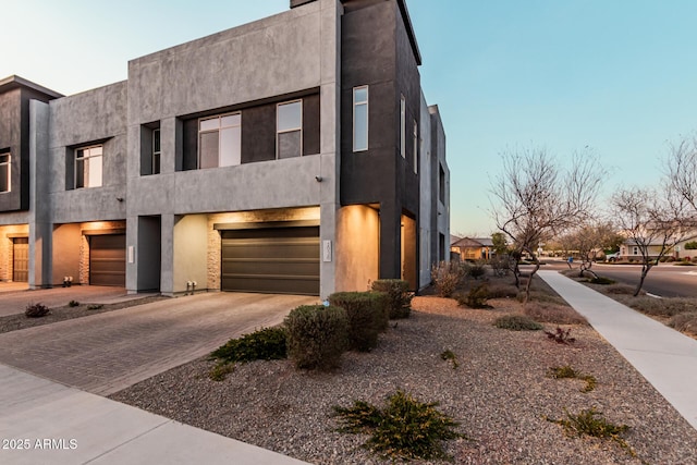 view of front of property with decorative driveway, an attached garage, and stucco siding