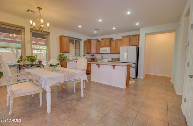 kitchen with hanging light fixtures, a notable chandelier, white appliances, a breakfast bar area, and light tile patterned flooring